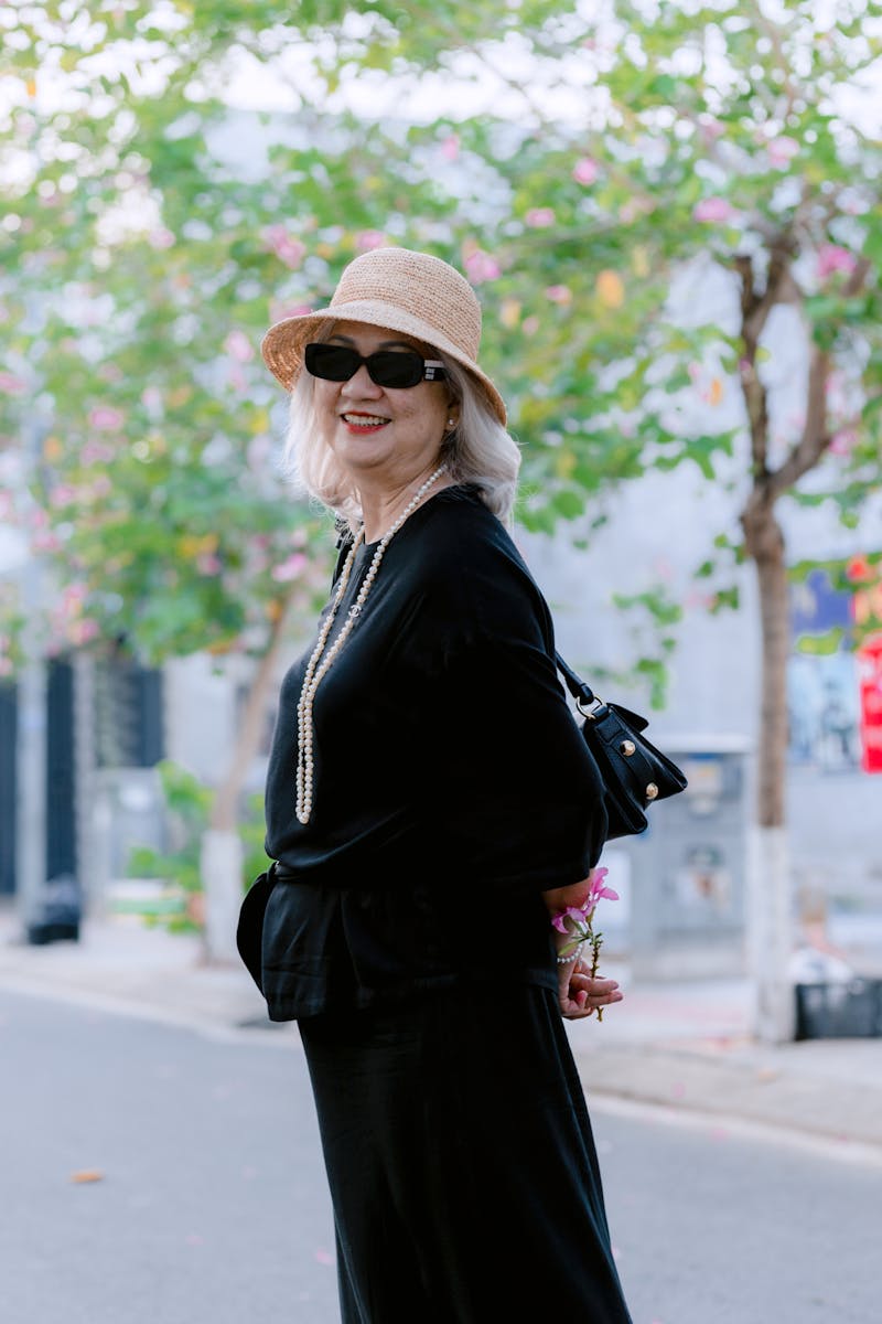 Elegant senior woman in black with hat and sunglasses on a sunny day.